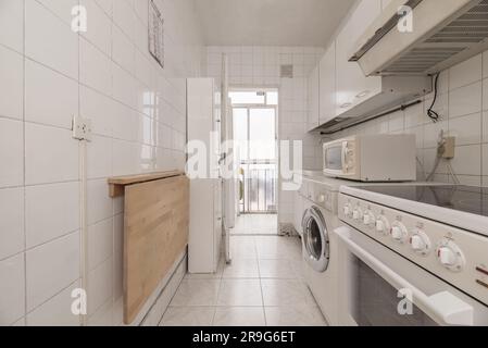 Old kitchen with mismatched white cabinets, white square tiles, walkout to a deck, and a wooden folding table against the wall Stock Photo