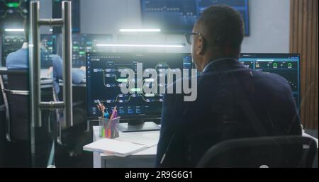 Technical support specialists sit at computers with displayed blockchain network map and server data. Big data scientists work in monitoring room. Big screens on the wall. Concept of cyber security. Stock Photo