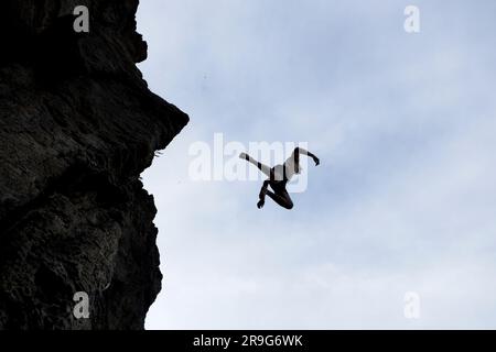 A silhouette of a young man jumping off a high rock into the water below in southern Idaho. Stock Photo