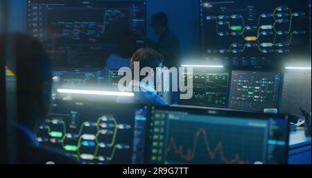 Technical support specialist types keyboard sitting at computer with displayed blockchain network map and server data. Big data scientists work in monitoring room late night. Cyber security concept. Stock Photo