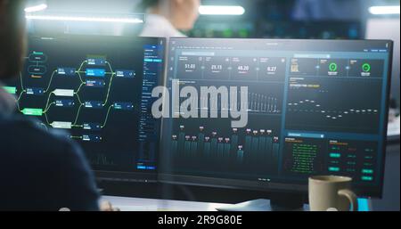 Female software engineer works on computer with data server and blockchain network database in modern monitoring control room. Team of IT technical specialist and big digital screens on background. Stock Photo