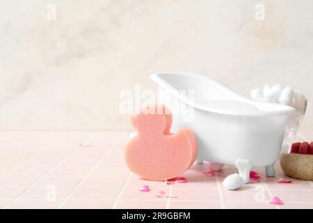 Small bathtub with foam, sponge, cotton balls and flower petals on color tile table Stock Photo