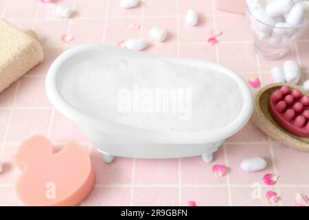 Small bathtub with foam and bath supplies on color tile background Stock Photo