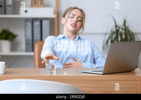 Young businesswoman taking glass of water with soluble tablet in office, closeup Stock Photo