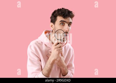 Shocked young man with magnifier on pink background Stock Photo