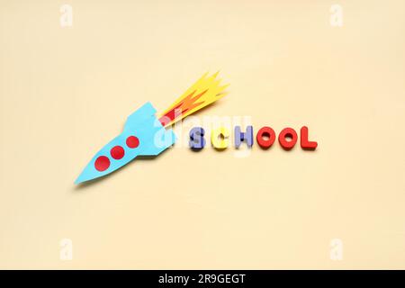 Paper rocket with word SCHOOL on beige background Stock Photo