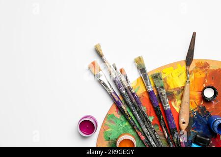 Wooden palette with different paints and brushes isolated on white background Stock Photo