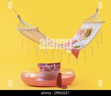 Cozy hammock with inflatable ring and different beach accessories on yellow background. Summer vacation concept Stock Photo