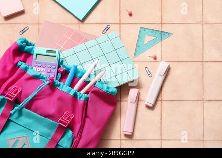 Colorful school backpack with notebooks, calculator and markers on beige tile background Stock Photo