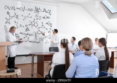 Professors giving lecture in chemistry to audience in conference room. Projection screen with different illustrations Stock Photo