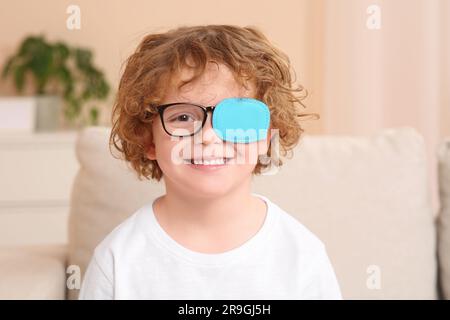 Happy boy with eye patch on glasses indoors. Strabismus treatment Stock Photo