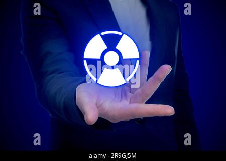 Woman holding glowing radiation warning symbol on dark blue background, closeup Stock Photo