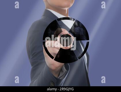 Woman drawing radiation warning symbol with marker on glass board against steel blue background, closeup Stock Photo