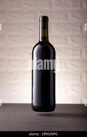 Unlabeled red wine bottle mockup floating on gray stone surface, white rustic brick wall background. Minimalist concept. Stock Photo