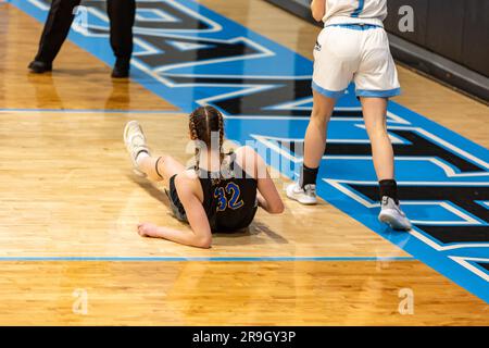 A  fallen player is on the floor after a play during a girls' high school basketball game in Auburn, Indiana, USA. Stock Photo