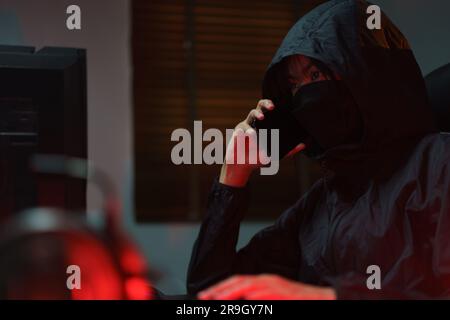 Hacker in hoodie talking on smartphone and typing code to hacking programming system or server. Stock Photo