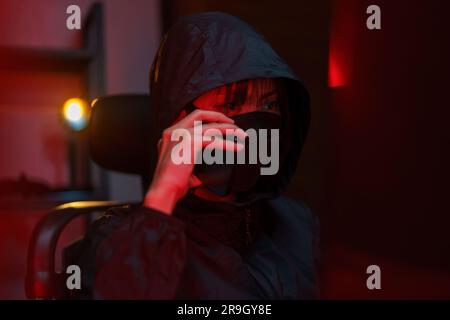 Hacker in hoodie talking on smartphone and typing code to hacking programming system or server. Stock Photo