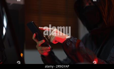 Hacker in hoodie using smartphone and computer to hacking programming system or data of server. Stock Photo