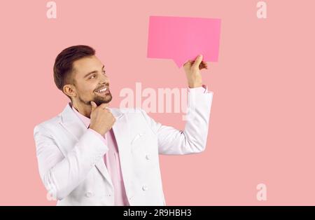 Happy young man holding blank pink message bubble, thinking about something and smiling Stock Photo