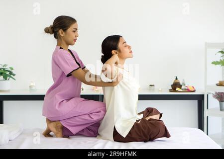 Cute girl with traditional dress stretch back and shoulder by massager. Young asian woman relax in spa. Body care treatment by thai massage performed Stock Photo