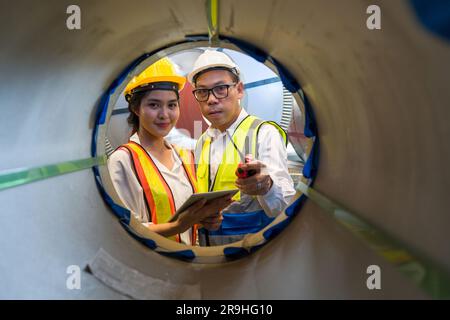 Asian male and female factory worker inspecting quality rolls of metal sheet in factory. Metalwork manufacturing, warehouse of raw materials. Stock Photo