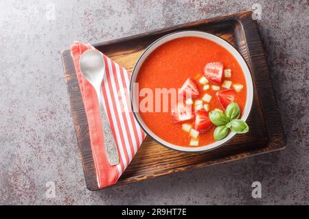 Cold summer tomato soup gazpacho with strawberries, cucumbers and basil close-up in a bowl on the table. Horizontal top view from above Stock Photo