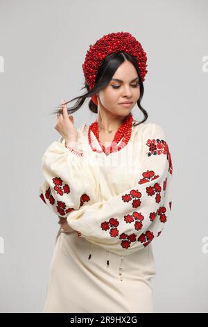 Vyshyvanka day in Ukraine. Beautiful young brunette woman dressed in Ukrainian traditional ethnic embroidered shirt, vyshyvanka, red wreath and necklaces at studio. Independence day, folk concept Stock Photo