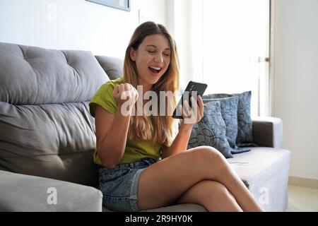 Young happy lucky woman feeling excited winner using mobile phone winning online, receiving great news or sms offer, getting new job celebrating achie Stock Photo
