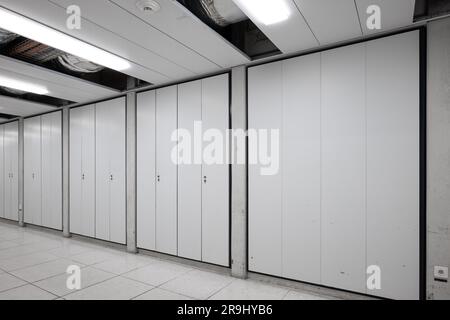 Long interior empty corridor hallway illuminated by neon lights with locker doors across both side, no people. Stock Photo