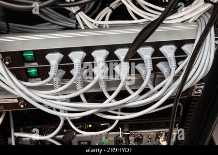 Neatly organized power cord extension cables with fully used plugs on an industrial rack. Indoors, no people. Stock Photo