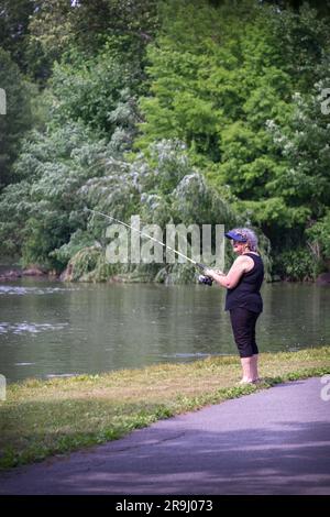 A middle aged woman fishes at the lake in Kissena Park, Flushing, Queens, New York, Summer, 2021 Stock Photo