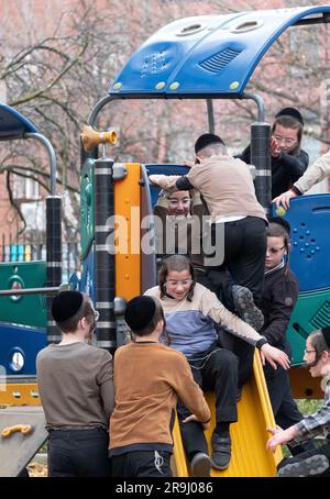 Playful orthodox Jewish children play on a sliding pond during recess at their yeshiva. In Brooklyn, New York Autumn, 2022. Stock Photo