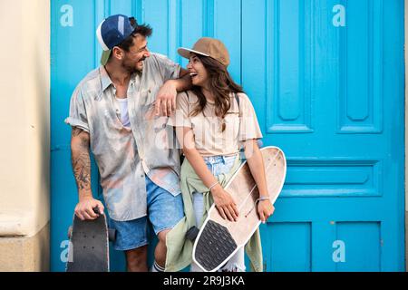 Tourists couple skateboarders riding skates. Happy young travelers longboarding together on sunset on pavement. Stylish man and woman in trendy outfit Stock Photo