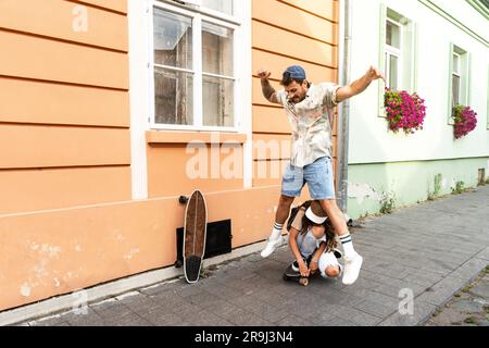 Tourists couple skateboarders riding skates. Happy young travelers longboarding together on sunset on pavement. Stylish man and woman in trendy outfit Stock Photo