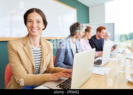 Smiling businesswoman using laptop while sitting by colleagues Stock Photo