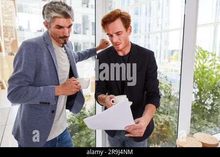 Male colleagues with coffee cups discussing over documents Stock Photo