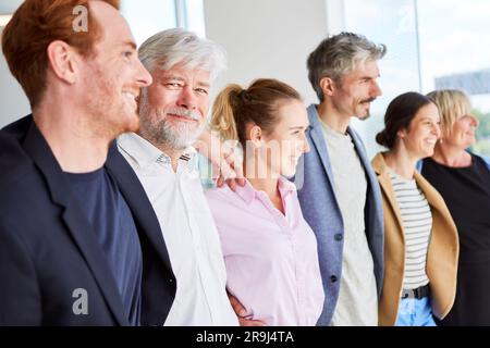 Smiling senior businessman standing with arms around colleagues Stock Photo