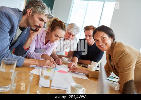 Smiling businesswoman discussing over documents and sticky notes with colleagues Stock Photo