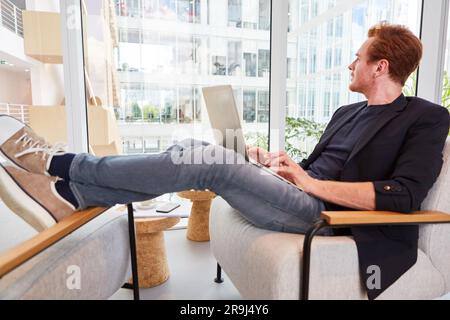 Thoughtful businessman using laptop while sitting with feet up on chair Stock Photo