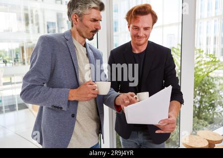 Confident male colleagues with cups discussing over documents Stock Photo