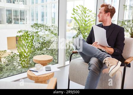 Thoughtful redhead male entrepreneur sitting with documents in lounge Stock Photo