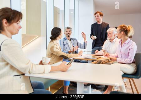 Confident businessman gesturing while discussing with colleagues in lounge Stock Photo