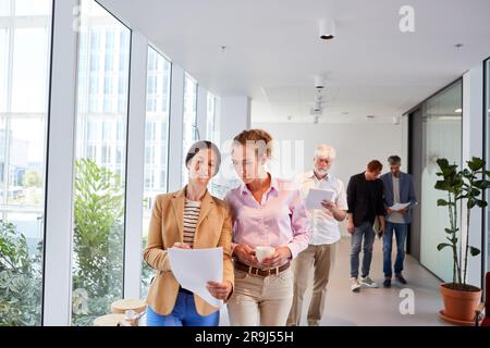Female entrepreneurs discussing over documents while walking in corridor Stock Photo