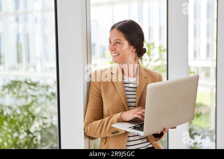 Happy businesswoman holding laptop day dreaming in lounge Stock Photo