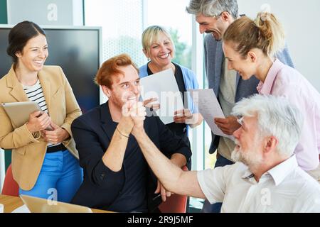 Happy team looking at businessman giving high five to successful colleague Stock Photo