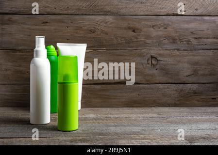 Blank green and white plastic container. Spray bottle and tube blank packaging standing on wooden background, copy space. Antiperpirant, repellent, an Stock Photo