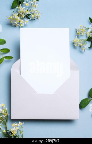 Greeting or invitation blank card in envelope, white delicate clematis flowers on blue gray background, copy space. Stylish creative mock up, romantic Stock Photo