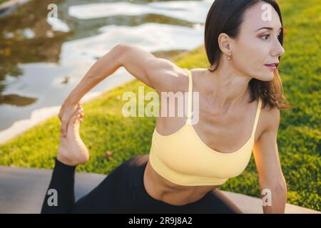 Side view of young female in sportswear sitting on haunches and looking away while resting on shore of lake Stock Photo