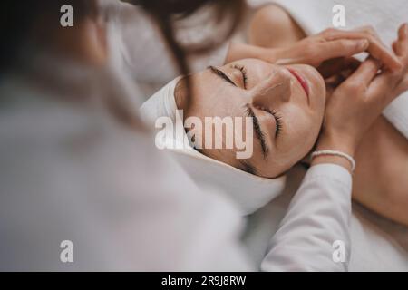 From above of crop anonymous female applying moisturizing cream on face while sitting in light room during skin care routine in morning at home Stock Photo