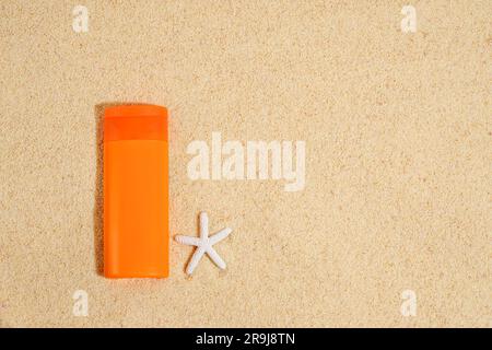 Sunscreen in orange plastic tube with white starfish on sand background . Sunscreen with UVA and UVB protection. Summer, sea Stock Photo